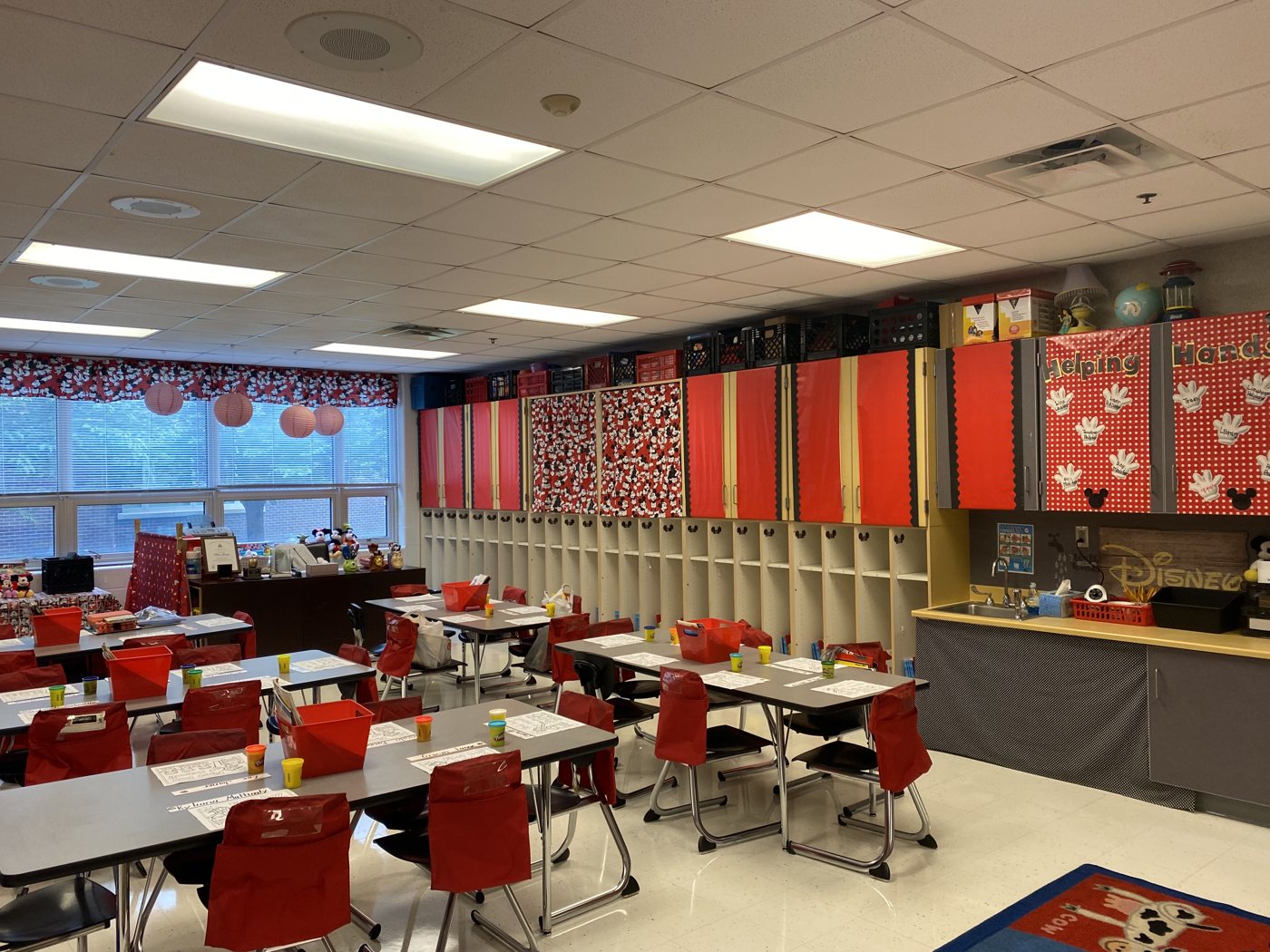Tables with red chairs and supply bins, red and white polka-dot cubbies along the wall.